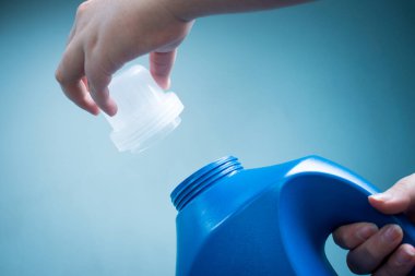 Mavi arka planda mavi sıvı sabun şişesini tutan el.