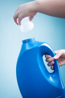 Mavi arka planda mavi sıvı sabun şişesini tutan el.