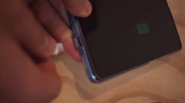 Beyaz şarj kablosuyla şarj olan cep telefonunun dikey videosu ahşap masada.