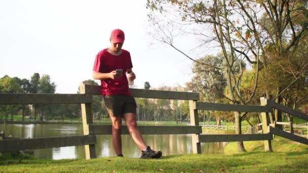 Uomo Con Cappuccio Rosso Acqua Potabile Dalla Bottiglia Nel Parco — Video Stock