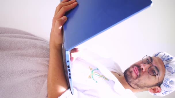 Vertikal Video Manusia Mengenakan Handuk Dan Topi Mandi Mencari Laptop — Stok Video
