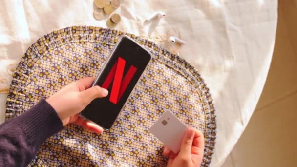 持信用卡并在屏幕上留下带有Netflix标志的智能手机的妇女 — 图库视频影像