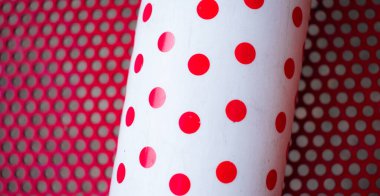 Kırmızı arka planda kırmızı noktalı beyaz şişe ve küçük delikler.