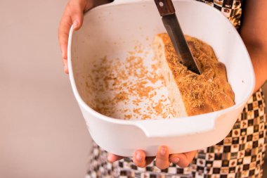 Önlük takan ve ekmek parçasında bıçak tutan bir kadın.