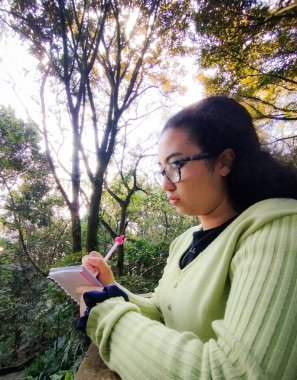 Ormanda deftere yazan genç bir kadın. 