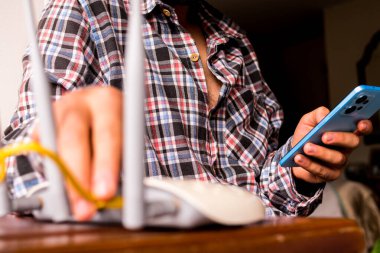 Telefonunu evdeki kablosuz internet yönlendiricisinin yanına bakan bir adam.