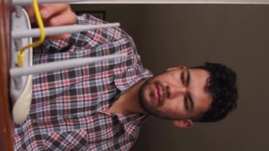 Evdeki kablosuz yönlendiricinin yanında telefonuna bakan adamın dikey videosu.