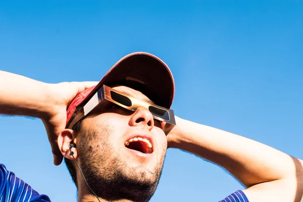 stock image Portrait of man wearing cap and solar eclipse glasses, looking sun with blue sky at background 