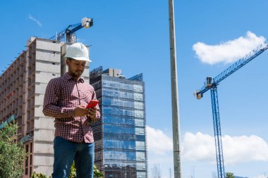 İnşaat işçisi güneşli bir günde telefonuna bakıyor.