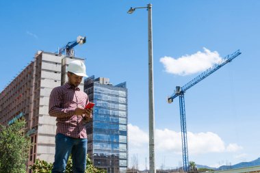 İnşaat işçisi güneşli bir günde telefonuna bakıyor.