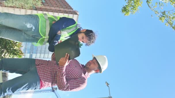 建設現場での取引のためのいくつかの文書を探している作業中の労働者の垂直ビデオ — ストック動画