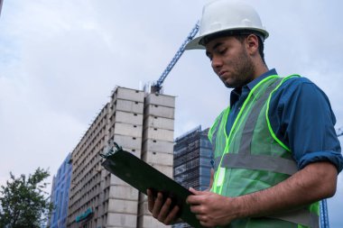 Güneşli bir günde inşaat sahasında belge arayan Latin inşaat işçisi.