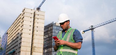 İnşaat işçisi güneşli bir günde telefonuna bakıyor.