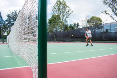 Yazın güneşli ve sıcak bir günde tenis oynayan genç adam.