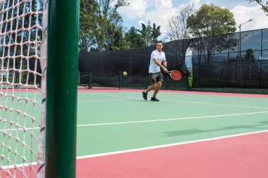 Yazın güneşli ve sıcak bir günde tenis oynayan genç adam.