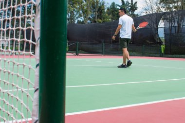 Yazın güneşli ve sıcak bir günde tenis oynayan genç adam.