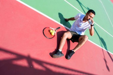 Genç latn tenisçisi güneşli yaz gününde tenis kortunda dinleniyor ve su içiyor.