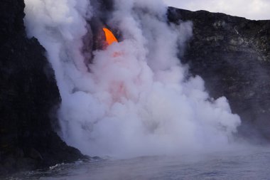Lava flowing down from high cliff into the ocean surrounded by white steam