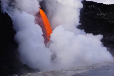 Lava flowing down from high cliff into the ocean surrounded by white steam