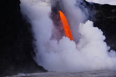 Lava flowing down from high cliff into the ocean surrounded by white steam