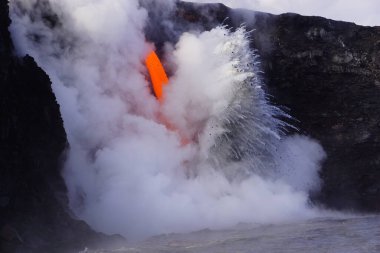 Lava flowing down from high cliff into the ocean surrounded by white steam