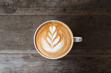 Ahşap arka planda kahve fincanı şeklinde kalp ağacı şeklinde Latte sanat kahvesi, sıcak içecek, masa üstü görünümü.