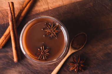 Tarçın çubuklu sıcak kakao, ahşap zemin üzerinde yıldız anason ve kakao tozu, kış mevsiminde sıcak içecek, masa üstü görünümü.