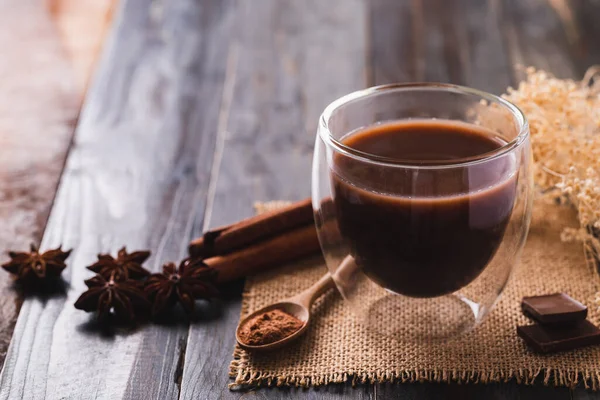 Hot cocoa in cup glass with chocolate, cinnamon stick, star anise and cocoa powder on wooden background, Hot drink in winter season
