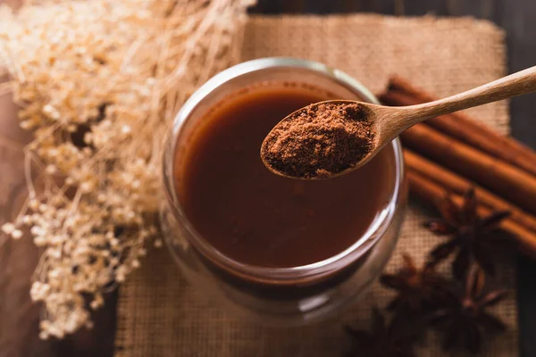 Hot cocoa in cup glass with cinnamon stick, star anise and cocoa powder in spoon, Hot drink in winter season