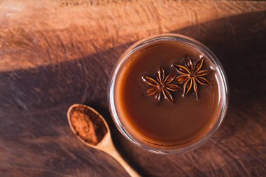 Bardakta sıcak kakao, yıldız anason ve ahşap arka planda kakao tozu kış mevsiminde sıcak içecek, masa üstü manzarası.