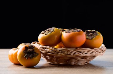 Tahta sepetteki taze hurma meyvesi siyah arka planlı, sonbahar mevsimlik meyvesi.