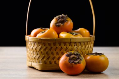 Tahta sepetteki taze hurma meyvesi siyah arka planlı, sonbahar mevsimlik meyvesi.