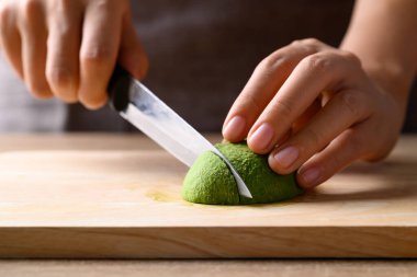 Olgun hass avokado meyvesi, elinde bıçak, tahtadan kesme, sağlıklı beslenme.