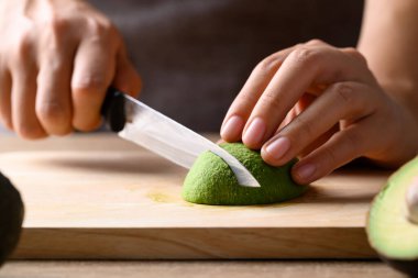 Olgun hass avokado meyvesi, elinde bıçak, tahtadan kesme, sağlıklı beslenme.