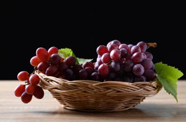 Kırmızı üzüm sepetinde siyah arka planlı ahşap masada.