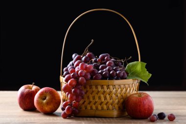 Ahşap masada siyah arka planda kırmızı üzüm ve elma meyvesi.