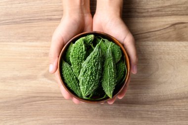 Ağaç zemin üzerinde elle tutulan acı kabak ya da acı kavun, Asya gıda malzemeleri ve bitkisel ilaçlar, masa üstü görünümü.