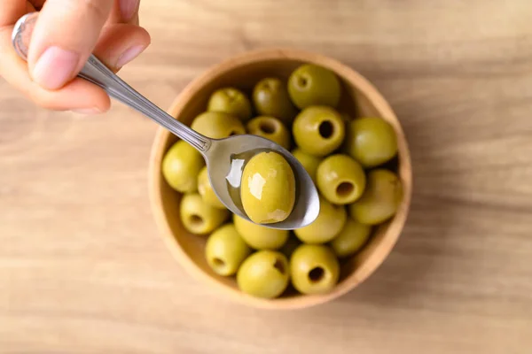 Pickled olives, Pitted green olives in spoon with hand, Table top view