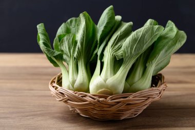 Tahta masa üzerinde siyah arkaplan ve organik sebzeler bulunan sepetteki bok choi veya Pak choi (Çin lahanası)