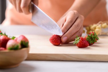 Mutfak bıçağı ve ahşap tahtada çilek kesmek.