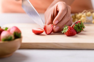 Mutfak bıçağı ve ahşap tahtada çilek kesmek.