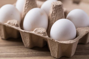 Tahta masadaki kağıt tepside, çiftlikten gelen organik beyaz leghorn yumurtası.