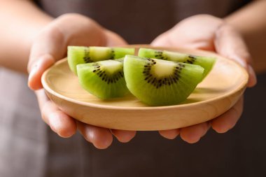 Tahta tabakta dilimlenmiş yeşil kivi meyvesi. Kadın eli, sağlıklı beslenme.