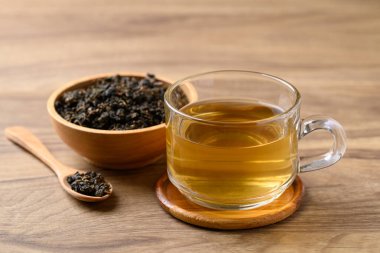Oolong çayı fincanda kurutulmuş Oolong çayı yaprakları ahşap arka planda, sağlıklı bir içecek.