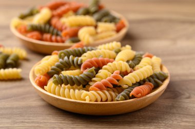 Sarı, turuncu ve yeşil fusilli makarna ahşap arka planda, yemek malzemesi