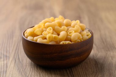 Ahşap arka planda kasede çiğ makarna, yemek malzemesi.