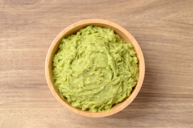 Ahşap arka planda kasede ezilmiş avokado, sağlıklı beslenme, masa üstü görünümü.