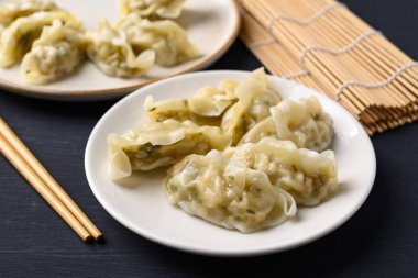 Domuz eti ve sebzelerle dolu buğulanmış hamur köftesi ve siyah arka planda yemek çubukları.