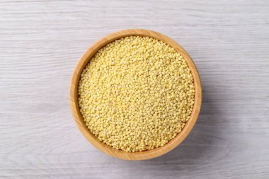 Beyaz masadaki ahşap kasede bulunan organik sarı darı tanecikleri sağlıklı besin malzemeleri, üst manzara.