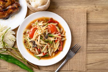 Baharatlı papaya salatası (Som Tum) yapışkan pirinç ve ahşap masada ızgara tavuk kanadı ile yenir.